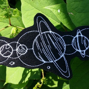 May include: A black felt patch with white embroidery depicting a stylized solar system with planets and stars.