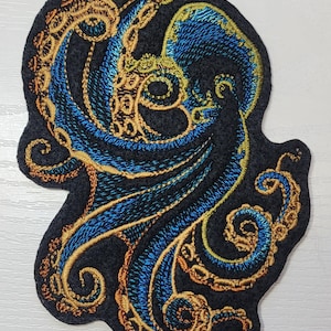May include: Embroidered patch of an octopus with blue and gold tentacles on a black felt background.