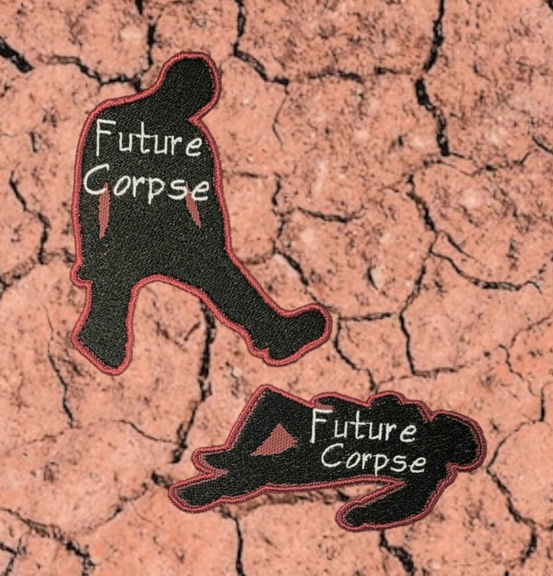 May include: Two black embroidered patches with red stitching. The patches are shaped like silhouettes of people. One patch shows a person standing with the text "Future Corpse" in white. The other patch shows a person lying down with the same text.