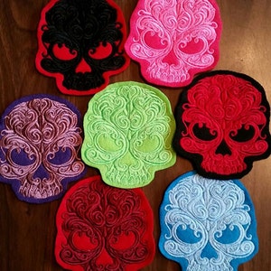 May include: Seven embroidered skull patches in various colors, including black, pink, purple, green, red, and blue. Each skull has intricate, swirling designs.