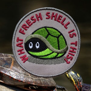 May include: A gray embroidered patch with a green turtle inside a shell. The text on the patch reads "What fresh shell is this?"