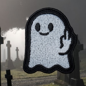 May include: A white ghost with a black outline and a mischievous smile is giving the middle finger. The ghost is embroidered on a black fabric patch.