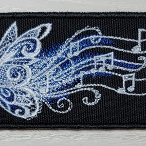 May include: A black embroidered patch with a white butterfly design. The butterfly's wings are made up of musical notes.