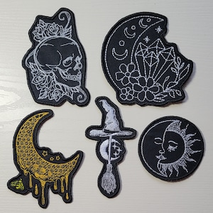 May include: Five embroidered iron-on patches with various designs. The patches are black with white embroidery. The designs include a skull with flowers, a crescent moon with a diamond, a witch's hat with a broom, a crescent moon with a sun, and a dripping honey moon.
