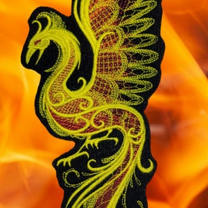 May include: A yellow and red embroidered patch of a phoenix with its wings spread. The phoenix is on a black background.