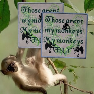 May include: Two embroidered patches with a light gray background and blue trim. The patches feature a green and black design with the text "Those aren't my monkeys. My monkeys fly."