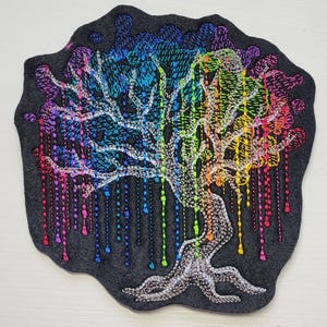 May include: A rainbow-colored embroidered patch of a tree with a white trunk and branches. The tree is on a black felt background.