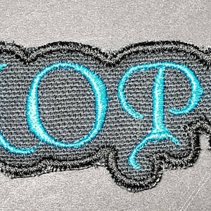 May include: Embroidered patch with the word "NOPE" in turquoise script. The letters are stitched onto a gray fabric background, framed by a black, wavy border. The patch is designed to be ironed or sewn onto clothing or accessories.