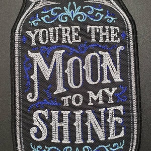 May include: A black and white embroidered patch with a mason jar design. The jar has a blue and white floral design and the text "You're the Moon to my Shine".