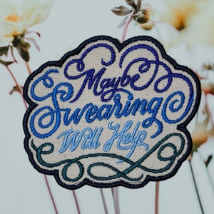 May include: A white embroidered patch with blue and green thread. The patch is shaped like a cloud and says "Maybe Swearing Will Help?"