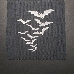 May include: A black fabric patch with a white silhouette of a flock of bats flying in a cluster.