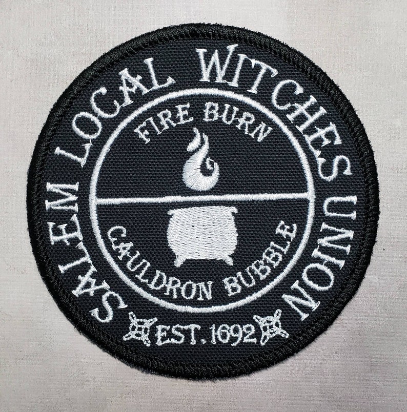 May include: Black and white embroidered patch with the text "Salem Local Witches Union" around the edge. The center of the patch features a cauldron with flames and the text "Fire Burn Cauldron Bubble Est. 1692".