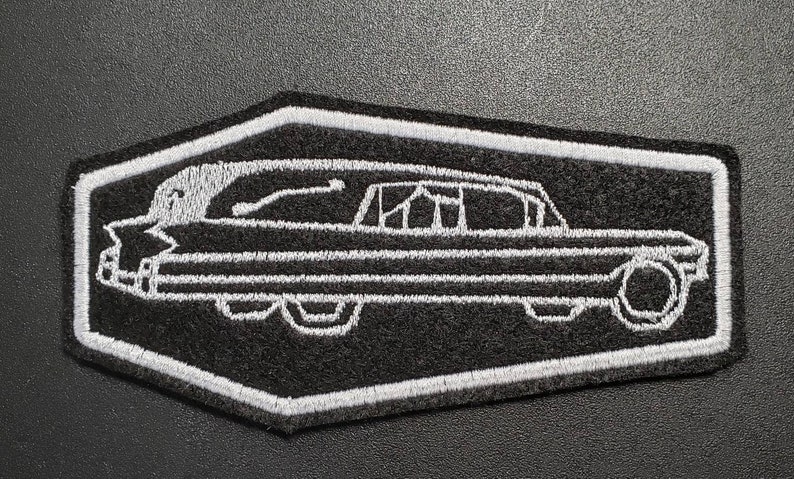 Pode incluir: Contorno branco bordado de um carro f&uacute;nebre vintage em um remendo preto. O remendo tem a forma de um hex&aacute;gono com cantos arredondados.