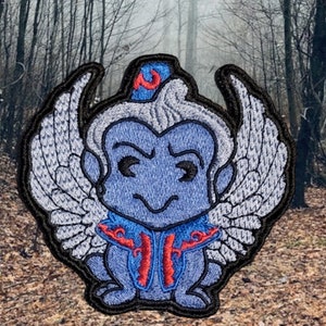 May include: Embroidered patch of a blue, winged monkey with a red and blue turban. The monkey has a mischievous expression and is wearing a blue and red robe.