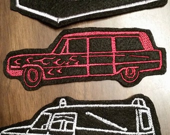 Op de afbeelding: Drie geborduurde patches met verschillende stijlen van rouwauto's. De eerste patch is zwart met een witte omtrek van een rouwauto in de vorm van een kist. De tweede patch is zwart met een rode omtrek van een rouwauto met vlammen aan de zijkant. De derde patch is zwart met een witte omtrek van een rouwauto met een dak.