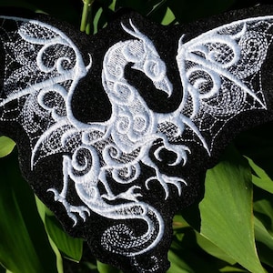 May include: White embroidered dragon design on a black fabric patch. The dragon is in a curled position with its wings spread out.