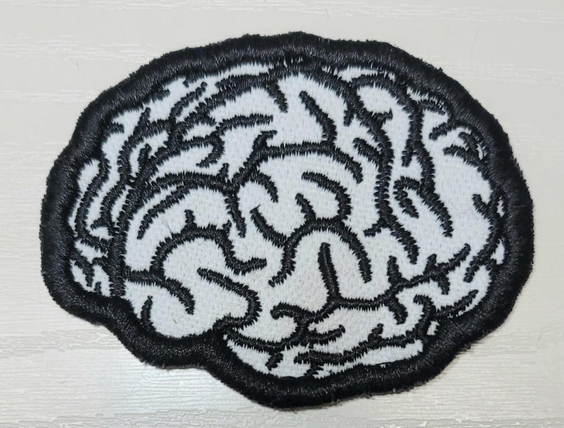 Pode incluir: Patch bordado em forma de c&eacute;rebro. O patch apresenta um fundo branco com linhas pretas bordadas que representam a estrutura do c&eacute;rebro. O patch &eacute; delineado com uma borda preta espessa.