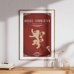 Peut inclure: Affiche encadrée avec le blason de la maison Lannister de Game of Thrones. L'affiche a un fond bordeaux avec un emblème de lion doré et les mots "House Lannister" et "Hear Me Roar" en blanc. Les mots "Game of Thrones" sont en bas.