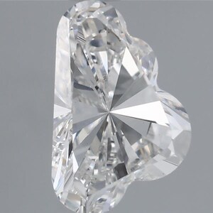 Könnte beinhalten: Ein klarer, herzförmiger Diamant mit vielen Facetten, der das Licht reflektiert. Der Edelstein hat einen Brillantschliff, der seine Klarheit und sein Funkeln zeigt. Die Herzform ist prominent.