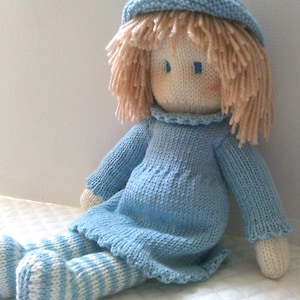 May include: A knitted doll with blonde yarn hair, a blue knitted hat, a blue knitted dress, and white and blue striped stockings.