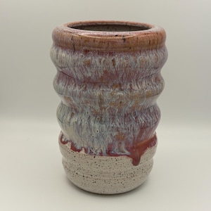 May include: A handmade ceramic vase with a textured, ridged design. The vase features a color gradient, transitioning from a speckled, off-white base to shades of red, pink, and brown at the top. The interior is a darker brown.