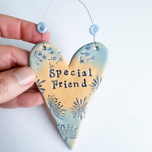 May include: A blue and yellow ceramic heart-shaped ornament with a white string for hanging. The heart has a blue and white floral pattern and the words "Special Friend" written in black.