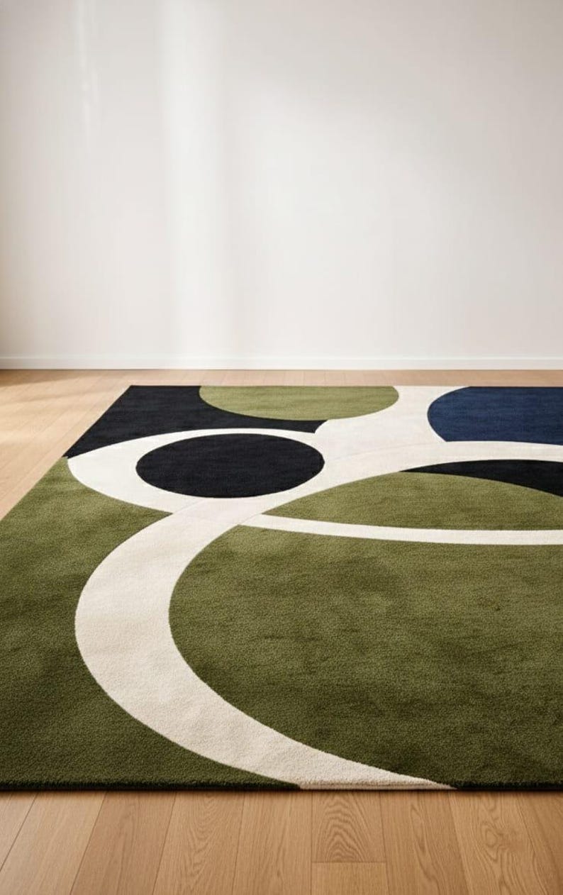 May include: A modern area rug with an abstract design. The rug features a green, black, navy blue, and white color palette. The design includes large circular and curved shapes. The rug is placed on a hardwood floor.