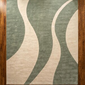 May include: A rectangular area rug with a flowing design. The rug features a light green background with three off-white, wavy stripes. The rug is placed on a wooden floor.