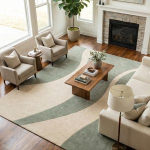 May include: An overhead view of a living room with a large area rug featuring a wavy design in cream and sage green. The room includes two armchairs, a sofa, a wooden coffee table, and a floor lamp.