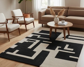 Puede incluir: Una alfombra rectangular con un patrón geométrico de alto contraste en negro y crema. El diseño consiste en formas rectangulares y líneas entrelazadas audaces que crean una composición abstracta y estructurada en toda la superficie.