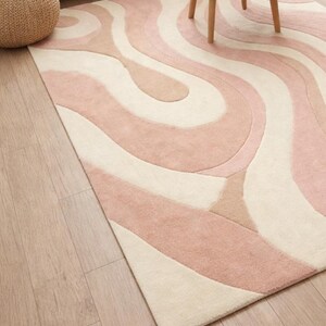 abstract wavy rug in pastel pink and cream
modern tufted rug for living room
soft wool area rug with curved design
hand tufted abstract rug on wooden floor
pastel color rug in cozy living space
modern home decor rug with wave pattern
minimalist area rug in cream pink tones
designer rug placed under coffee table
luxury wool rug for modern interiors
art inspired abstract floor rug
contemporary rug for stylish living room
soft texture tufted wool rug