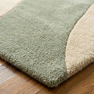 May include: Close-up of a soft, textured rug with a wavy design. The rug features a light green section and a beige section, creating a contrasting pattern. The rug is placed on a wooden floor.