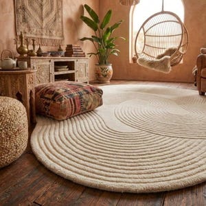 Puede incluir: Un salón acogedor con una gran alfombra redonda de color crema con un diseño ondulado. La habitación cuenta con una silla colgante de mimbre, un puf estampado y una gran planta en maceta. Las paredes están pintadas en un tono cálido y terroso.