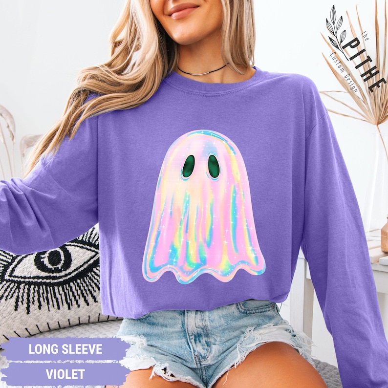 May include: A violet long-sleeve shirt featuring a holographic ghost graphic with green eyes. The shirt has the words "LONG SLEEVE" and "VIOLET" printed on a banner at the bottom. The shirt is a comfortable fit.