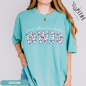 K&ouml;nnte beinhalten: T&uuml;rkisgr&uuml;nes T-Shirt mit dem Text "Love one another as I have loved you" &uuml;ber den Buchstaben "WWJD". Die Buchstaben sind mit einem Blumenmuster in Rot, Blau und Wei&szlig; gef&uuml;llt. Das Shirt hat eine lockere Passform.