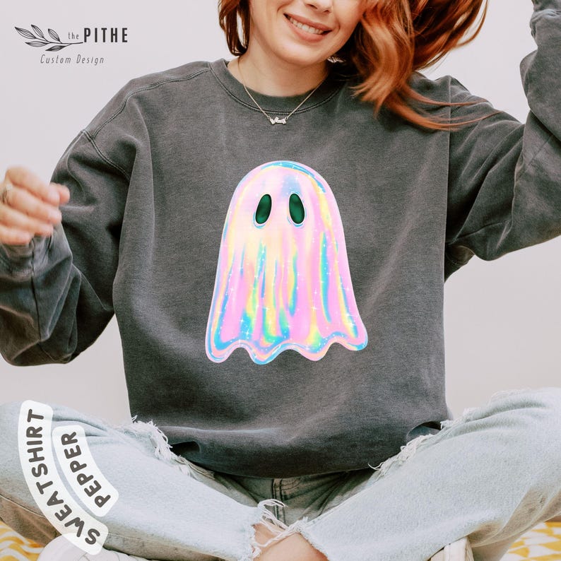 May include: Dark gray sweatshirt featuring a holographic ghost design with green eyes. The ghost has a shimmering, iridescent appearance with pink, blue, and yellow hues. The sweatshirt has the text "SWEATSHIRT PEPPER" on the bottom.