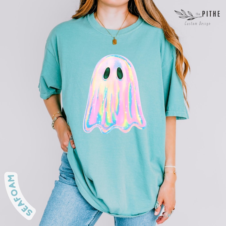 May include: Seafoam green t-shirt featuring a holographic ghost graphic. The ghost has a pearlescent, iridescent appearance with black oval eyes. The text "the PITHE Custom Design" is visible in the upper right corner. The word "SEAFOAM" is printed on the left side of the shirt.