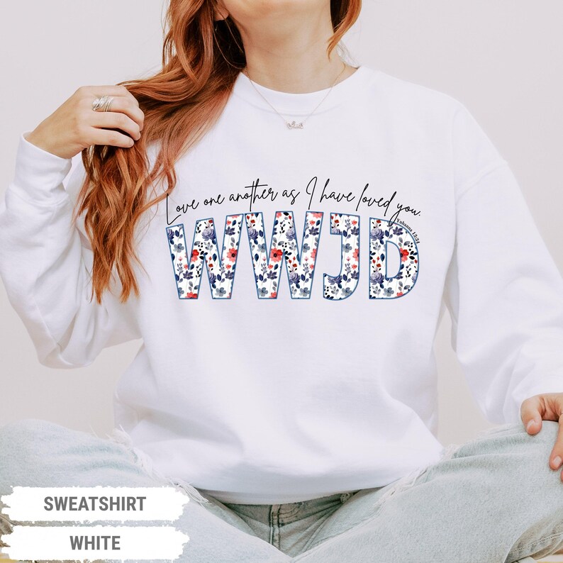K&ouml;nnte beinhalten: Wei&szlig;es Sweatshirt mit dem Text "Love one another as I have loved you" und "WWJD" in floralem Design. Das Sweatshirt ist ein lang&auml;rmeliger Rundhalsausschnitt.