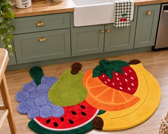 May include: A colorful, shaped area rug featuring a cluster of fruit designs including a purple grape bunch, a green pear, a red watermelon slice with black seeds, an orange slice, a red strawberry, and a yellow banana arranged in a large pattern.