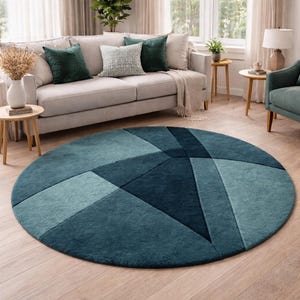 May include: A round teal rug with a geometric design in shades of teal and blue. The rug is placed on a light wood floor in a living room setting. The rug's design features angular shapes.