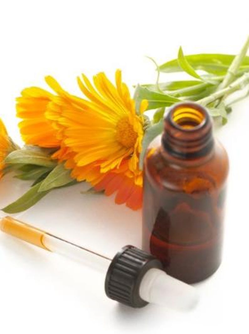 May include: A brown glass essential oil bottle with a dropper, next to bright orange calendula flowers and green leaves. The dropper is clear with a yellow liquid inside. The bottle has a black cap and white tip.