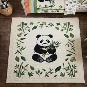 May include: A cream-colored rug with a panda bear design, surrounded by bamboo and leaves. The rug is in a child's room, with a matching bedspread, bookshelf, and toys.