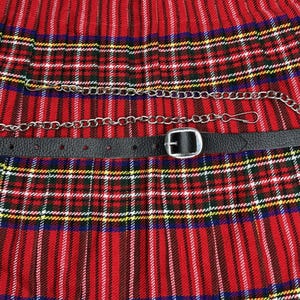 May include: A black leather belt with a silver buckle and a silver chain, set against a red, green, and yellow plaid fabric. The belt has multiple holes for adjustment. The chain is attached to the belt.