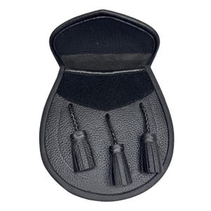 May include: Black leather sporran with three decorative tassels. The sporran has a textured front and a flap closure. The top of the sporran is a smooth black material.