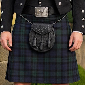 May include: A traditional Scottish kilt in a blue and green plaid pattern. The kilt is worn with a black jacket, a belt with a silver buckle, and a black leather sporran with tassels. The outfit is completed with black socks.