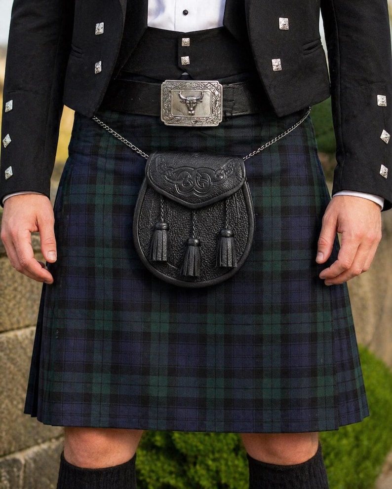 May include: A traditional Scottish kilt in a blue and green plaid pattern. The kilt is worn with a black jacket, a belt with a silver buckle, and a black leather sporran with tassels. The outfit is completed with black socks.