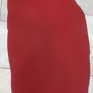May include: A solid red piece of leather, possibly for crafting or upholstery. The material is a deep, vibrant red, and the shape is irregular, suggesting it may have been cut from a larger hide. The surface appears smooth.