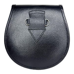 May include: A black leather sporran with a textured surface. The sporran has a rounded bottom and a flap closure with two silver-colored metal rings. The flap has a triangular design stitched into it.