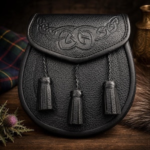 May include: A black leather sporran with a Celtic knot design embossed on the flap. The sporran has a rounded shape with three black tassels hanging from the bottom. The background includes a tartan fabric and a thistle.