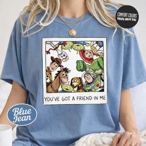 A person wearing a blue t-shirt with a graphic of characters from the Toy Story franchise, including Woody, Buzz Lightyear, and other beloved characters, along with the text "You've Got a Friend in Me".
